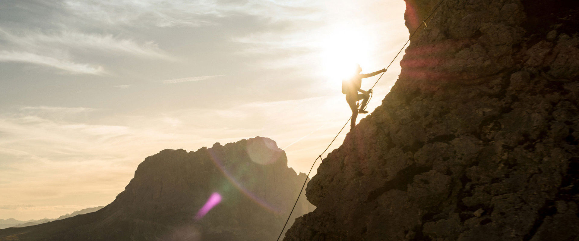 Un uomo si aggrappa alla corda della via ferrata e salendo piano la montagna.