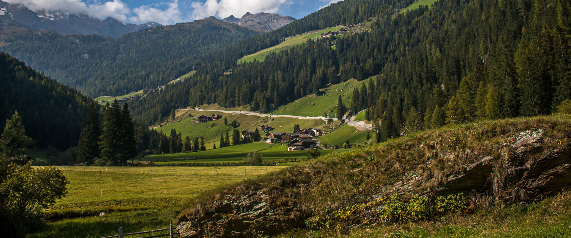 Val d’Ultimo Paesaggio montano con pendii boscosi, strada e case sparse.