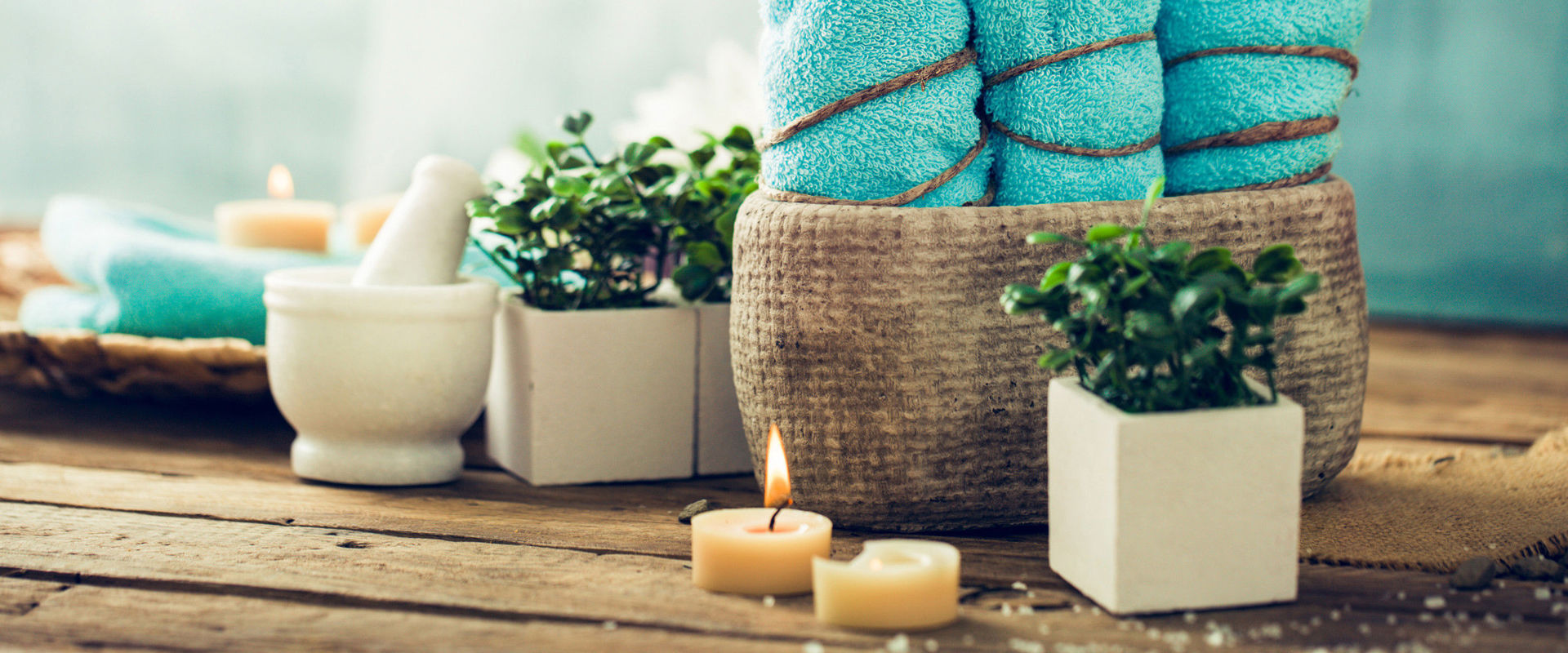 Prodotti per il benessere 3 asciugamani turchesi, candele e fiori su una base di legno.