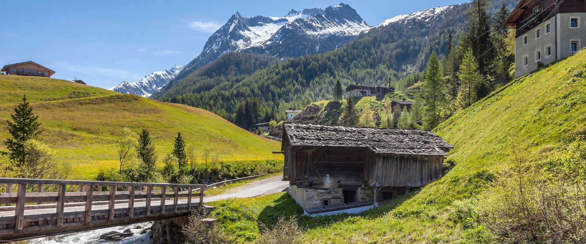Mondo alpino della Val Aurina Diverse baite in un paesaggio montano con ruscello e ponte di legno.