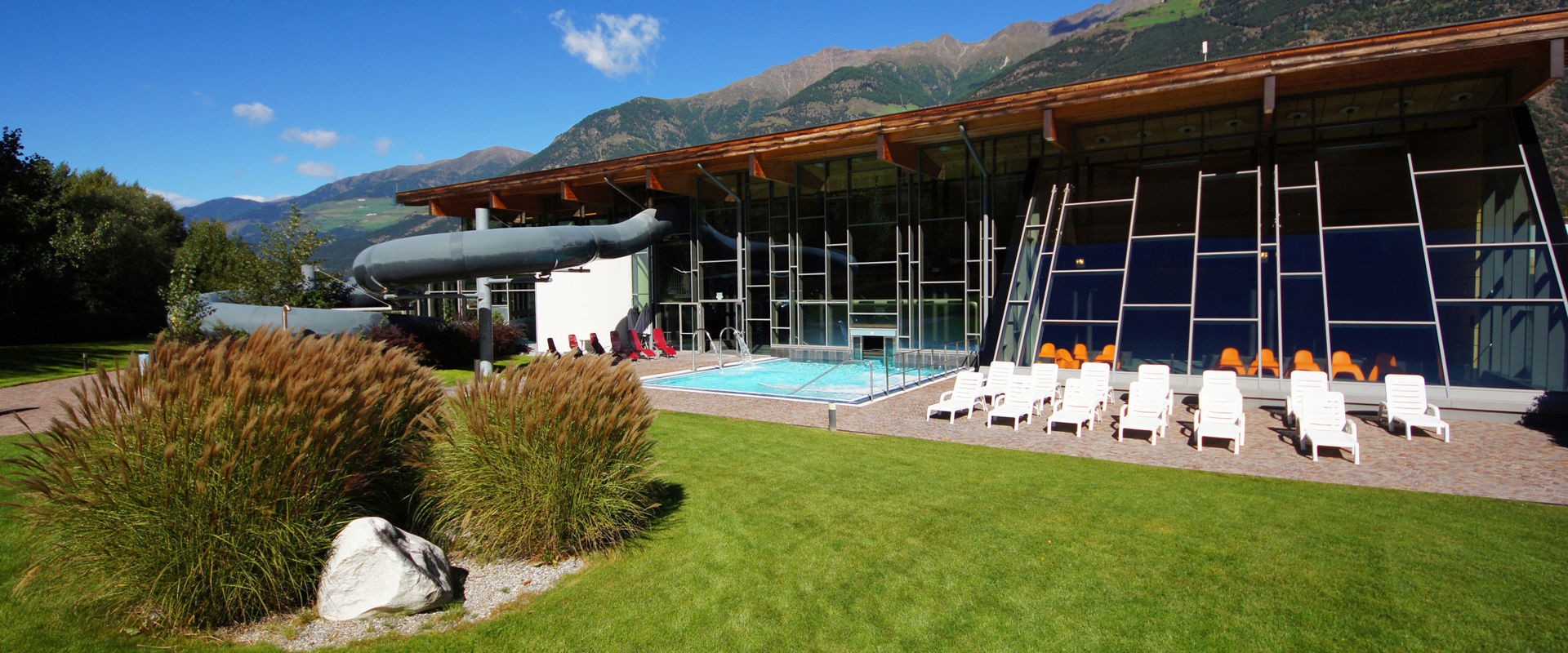 Vista della piscina di Laces con prato per amanti del sole, scivolo e piscina all'aperto.