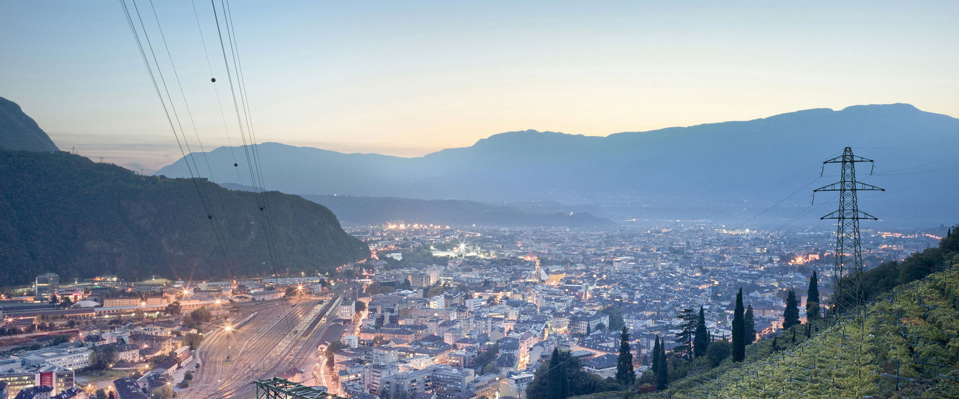 Città illuminata di prima sera e circondata da vigneti.