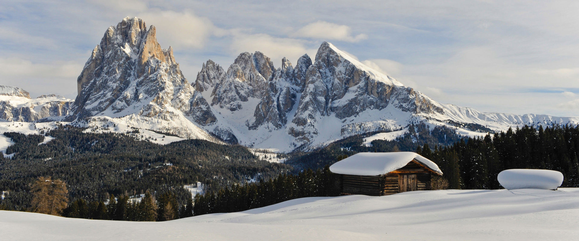 Inverno sull'Alpe di Siusi Panorama invernale con capanna di legno innevata e cime bianche.