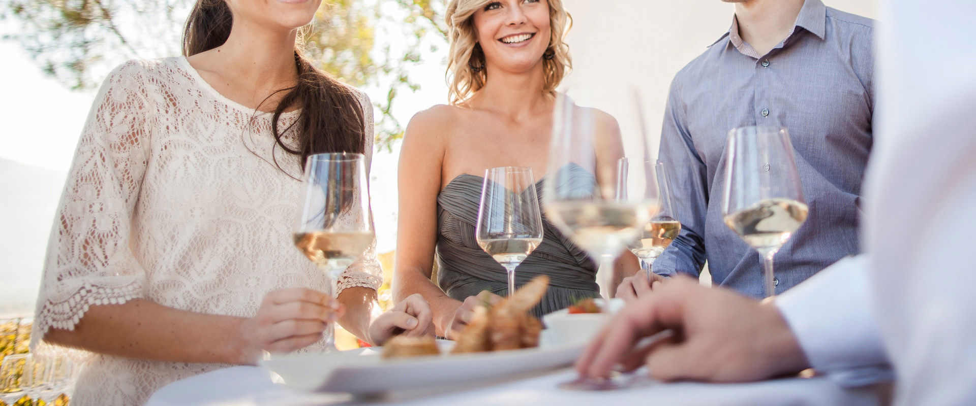 Gewürztraminer Alcuni giovani sono intorno a un tavolo con un bicchiere di vino bianco in mano.