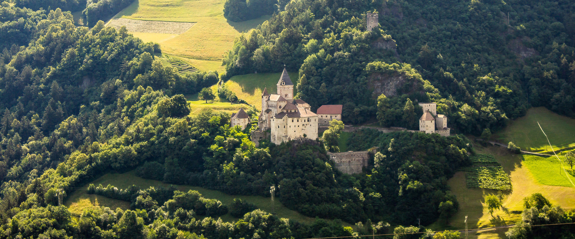 Castel Trostburg Castel Trostburg troneggia su un pendio in mezzo a prati verdi, campi e alberi.