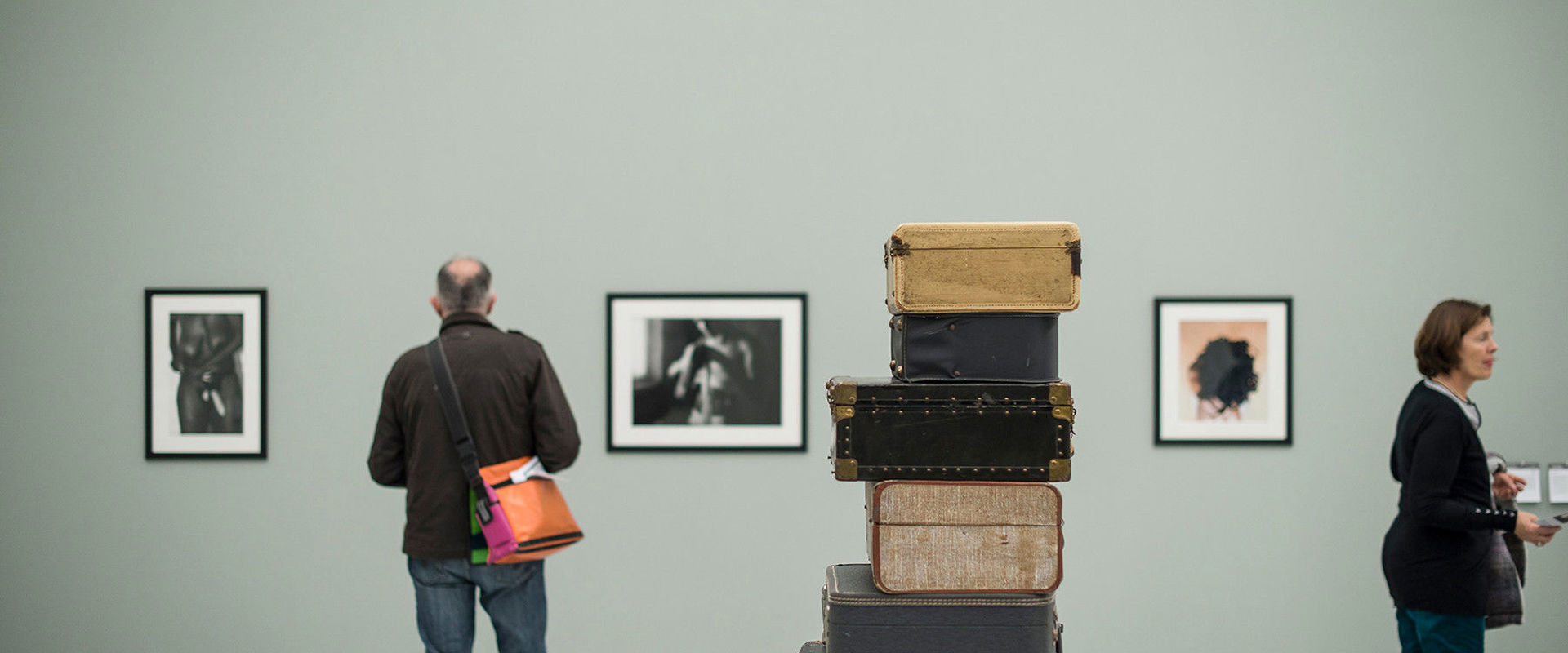 Museion Diverse vecchie valigie giacciono una sull'altra al centro della stanza. Alle pareti sono appesi dei quadri che vengono esaminati da due visitatori.