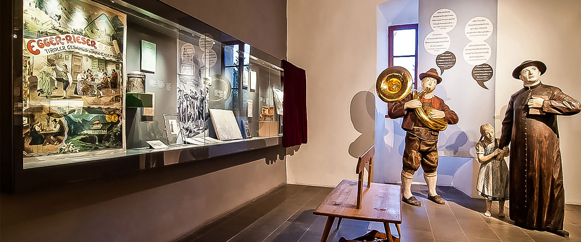 Figure umane in legno e una vetrina con vari oggetti rurali.