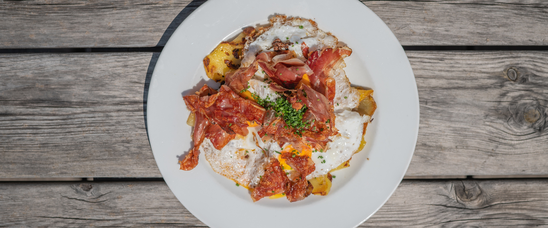 Piatto su un tavolo di legno con patate arrosto, speck e uova