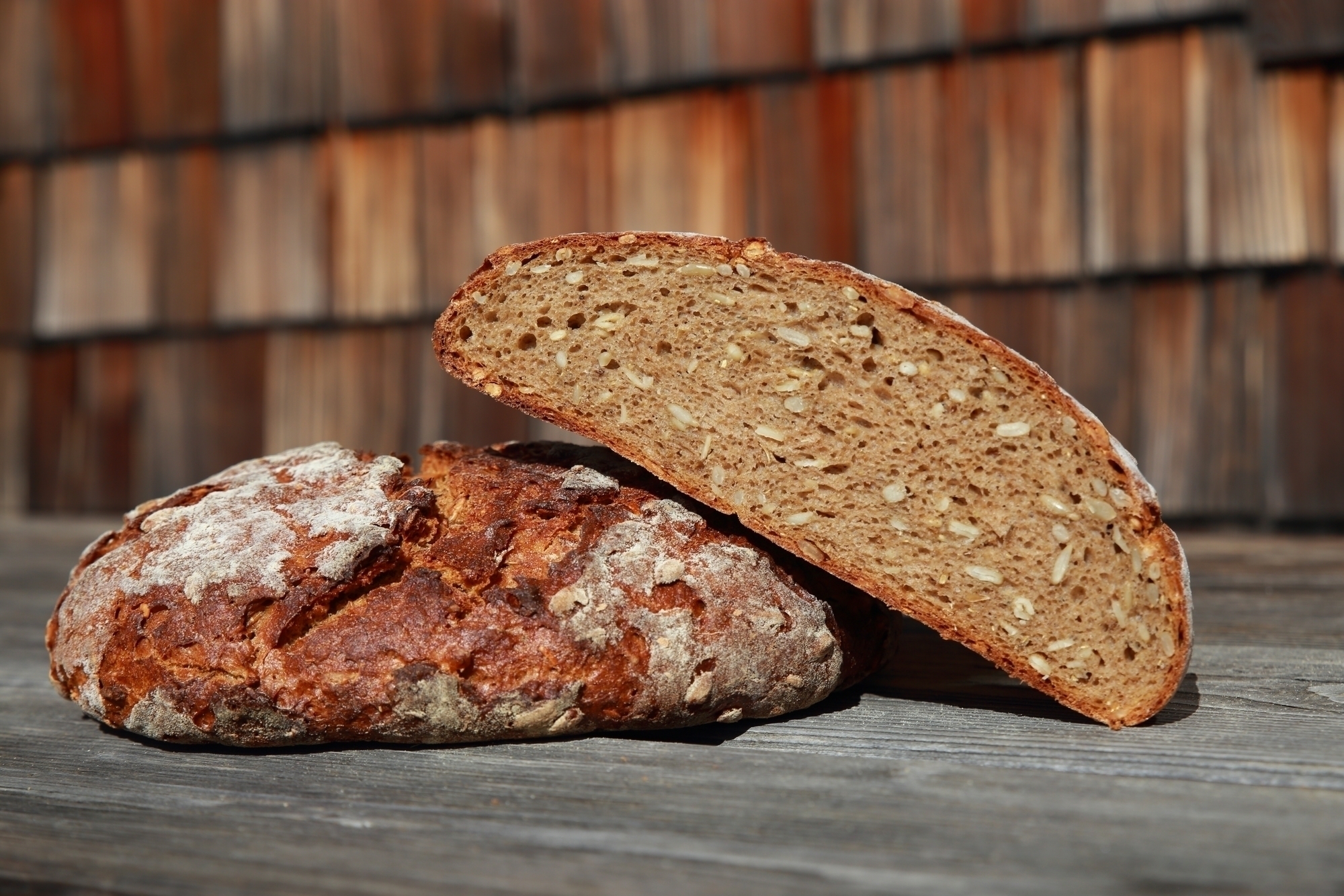 Una pagnotta intera e una mezza di pane cotto nel forno a legna sono appoggiate su un tavolo di legno davanti al rifugio Brixner Hütte.