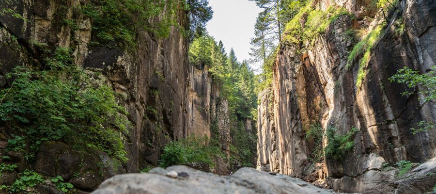 A sinistra e a destra dell'immagine, si vedono pareti rocciose rossastre in forte ascesa, ricoperte da alcuni alberi.