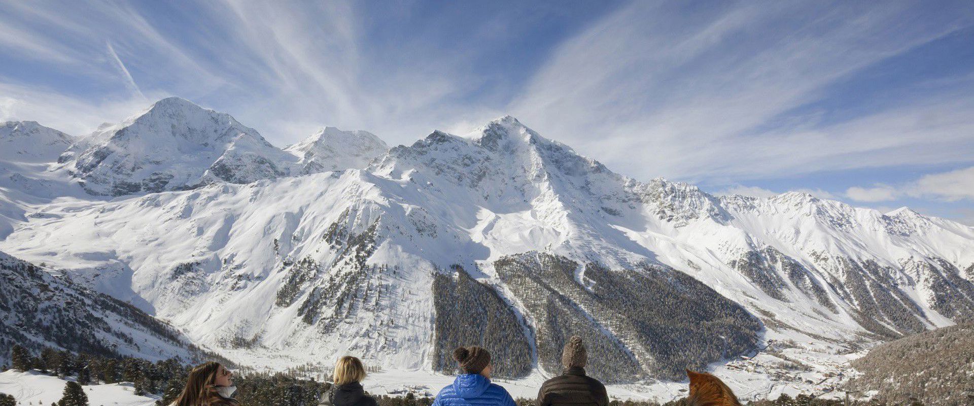 Parco Nazionale dello Stelvio in inverno Gruppo di giovani ragazze con cane sedute sulla neve in cima alla montagna, ammirando le vette innevate.