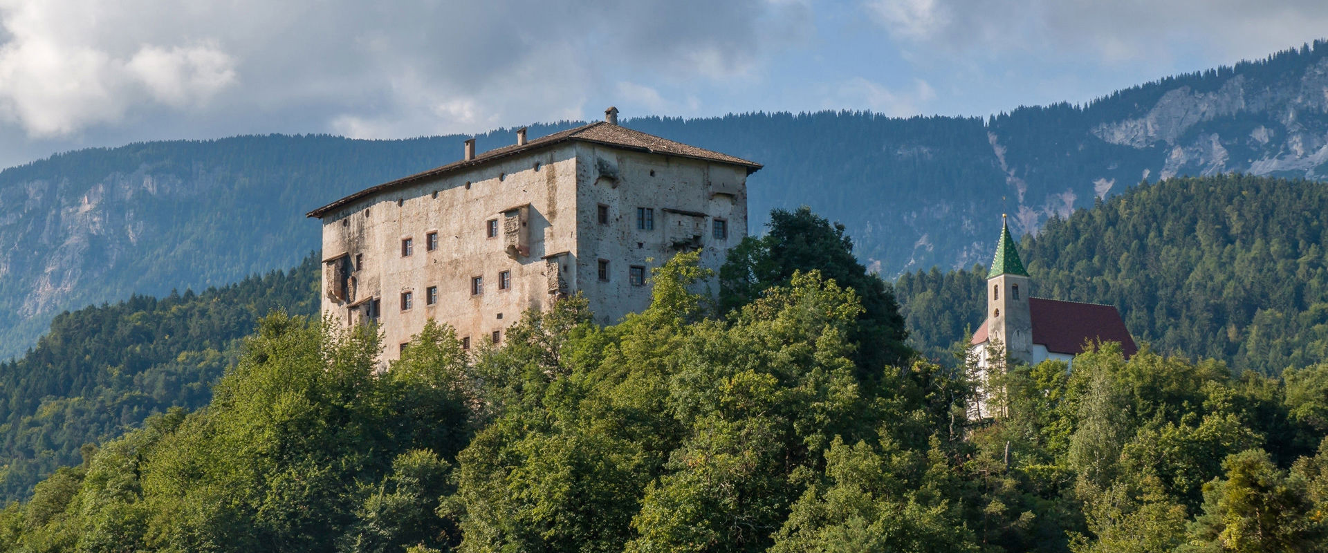Castello di Katzenzungen a Prissiano. Castello su una collina boscosa con accanto una chiesa.