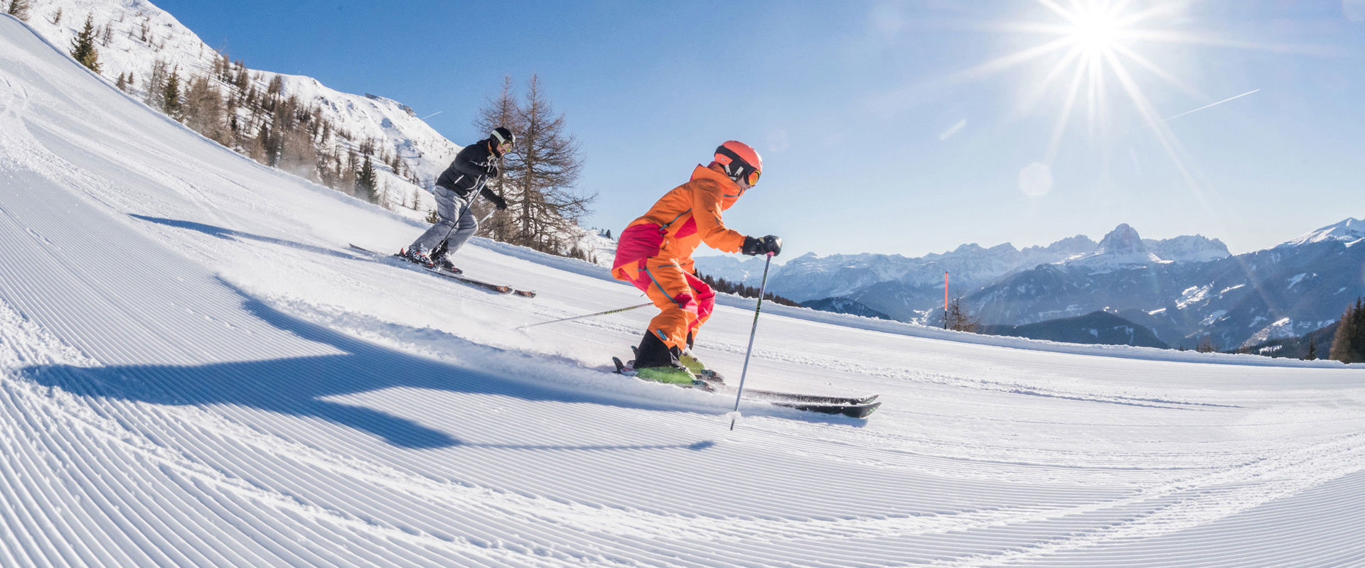 Pista da sci appena preparata 2 sciatori scendono lungo la pista appena battuta.