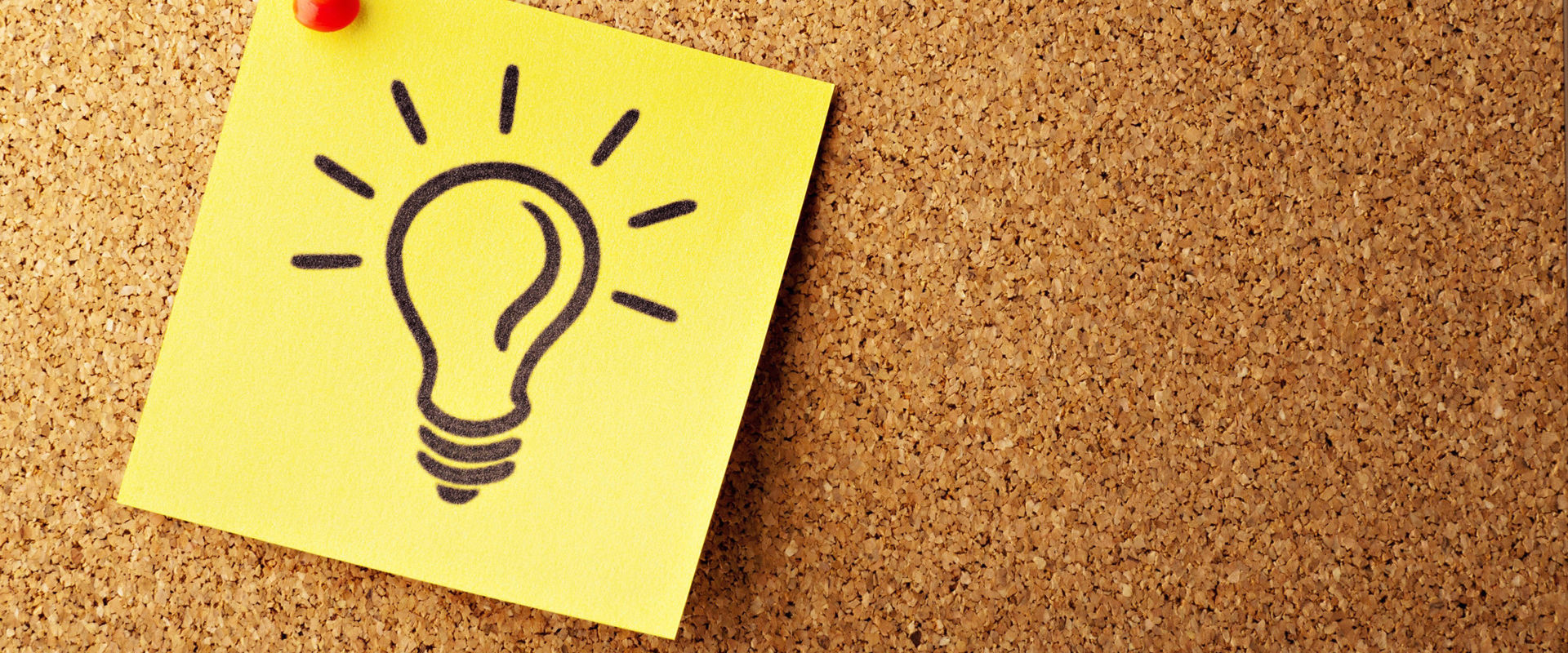 Un post-it con disegnato su una lampadina è appeso ad una parete di sughero.