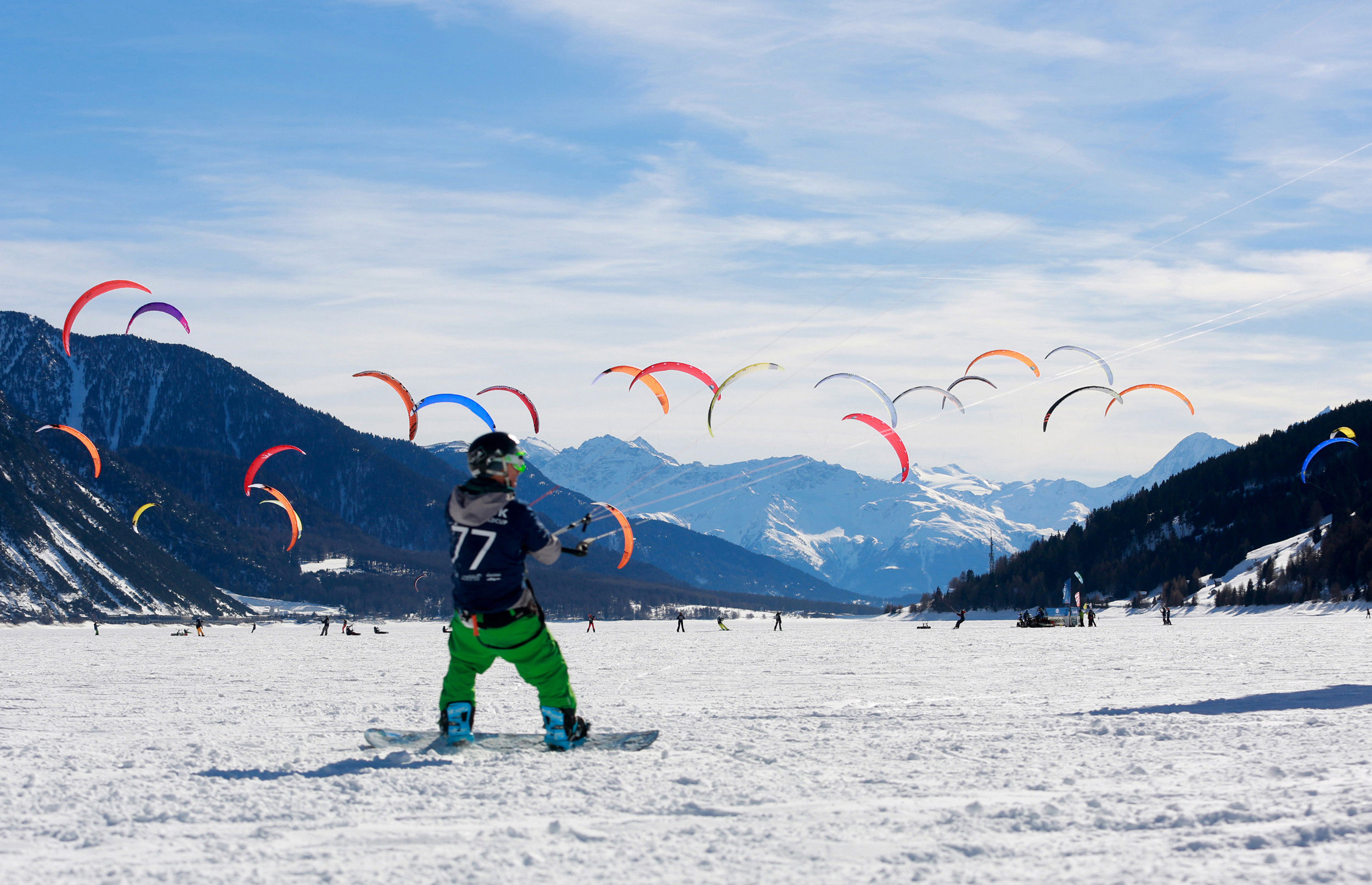 Snowkiters sul lago di Resia innevato.