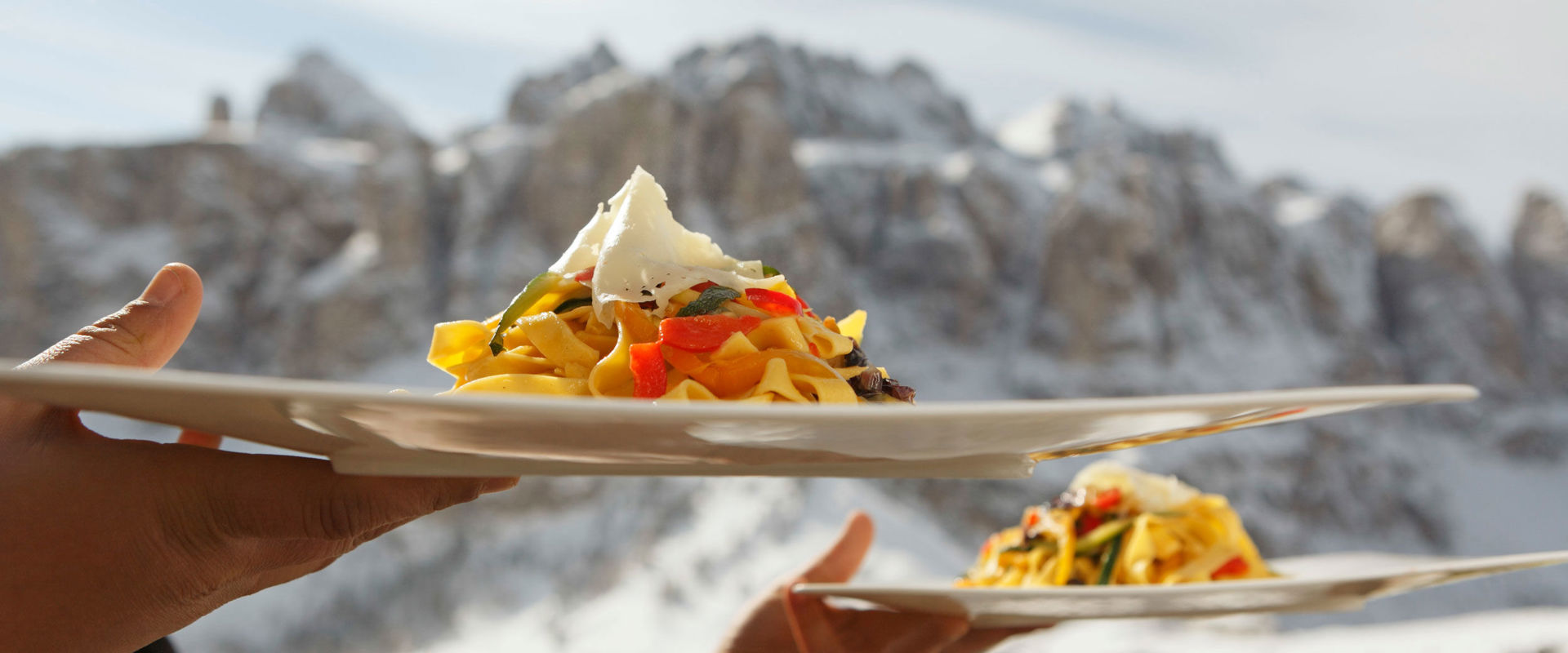 Mangiare con un'atmosfera invernale. Un cameriere serve 2 piatti di pasta davanti a uno sfondo di montagne innevate.