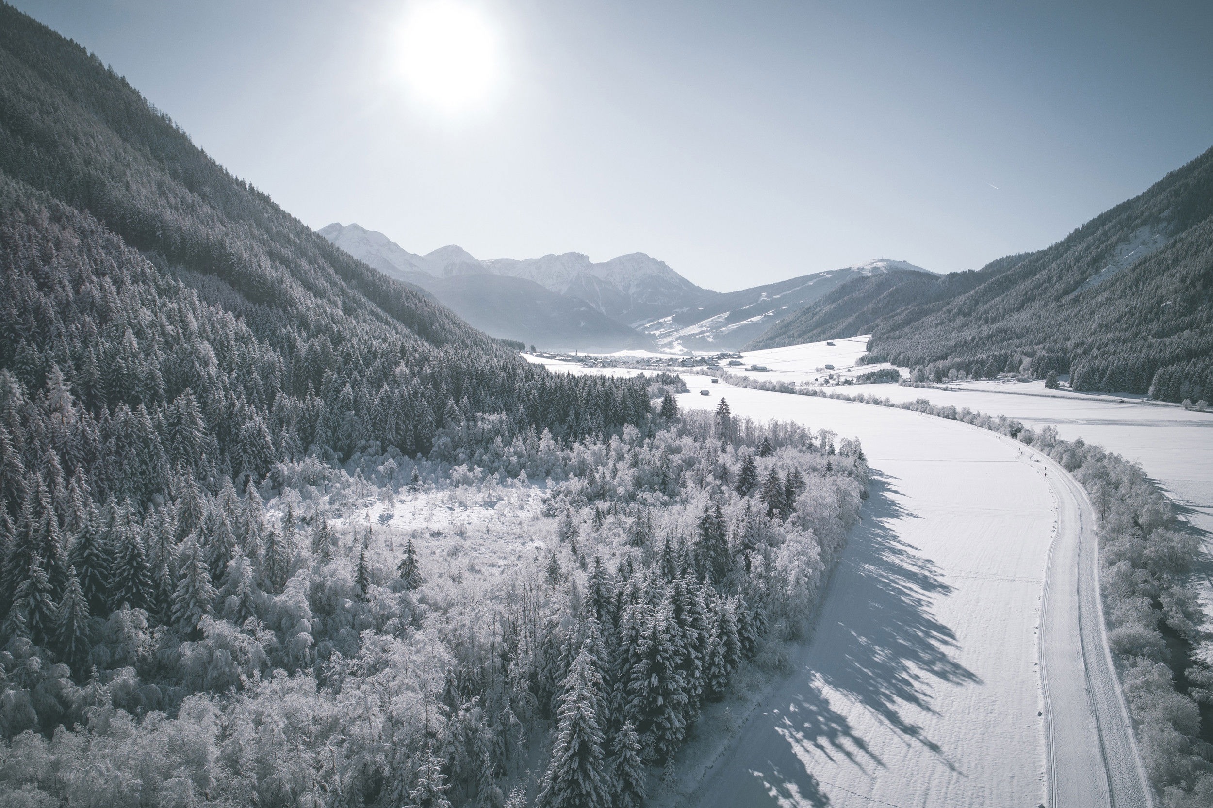 Veduta di una valle innevata e soleggiata con la pista da sci di fondo, sullo sfondo si vede un villaggio.