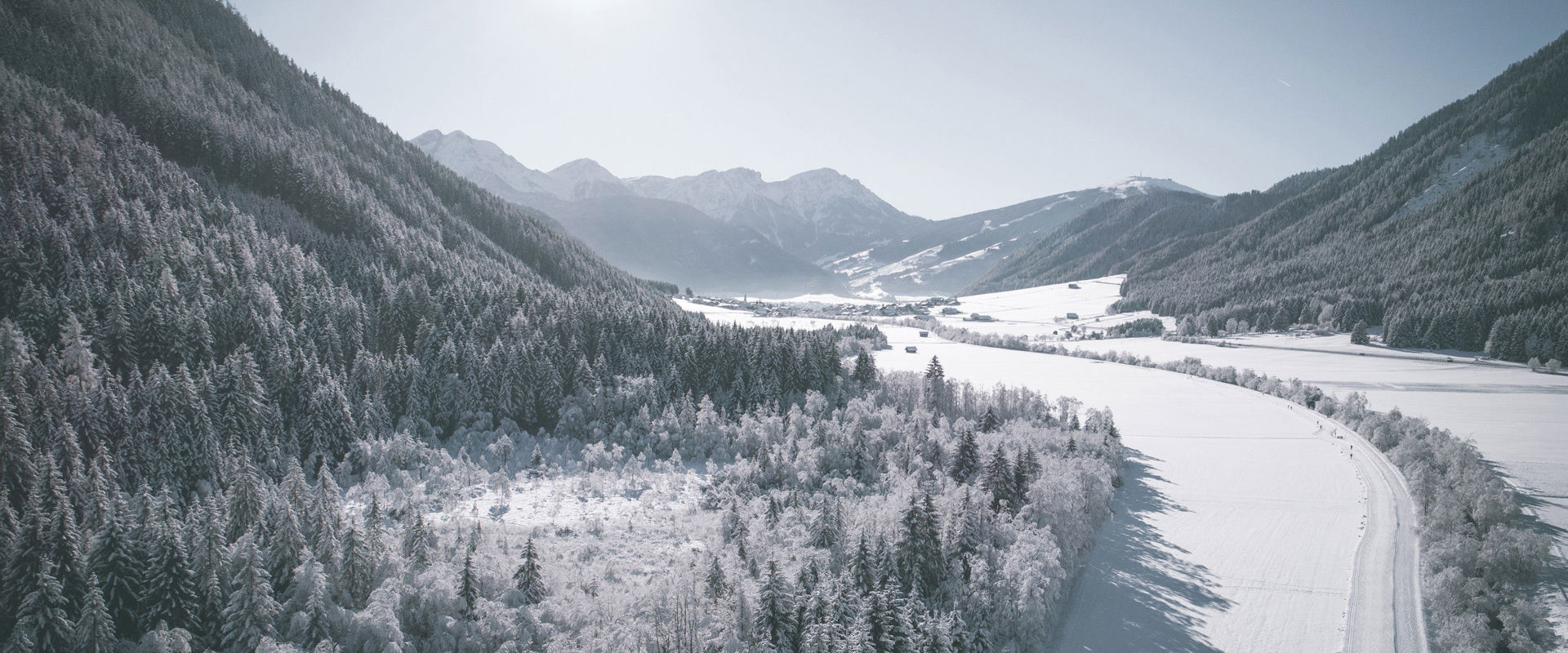 Inverno nella Valle di Anterselva. Veduta di una valle innevata e soleggiata con la pista da sci di fondo, sullo sfondo si vede un villaggio.