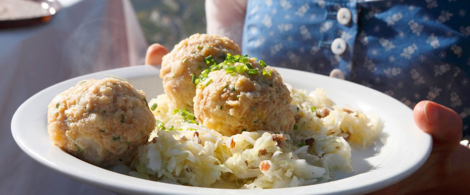 Canederli Una cameriera serve 3 canederli e insalata di cavolo.