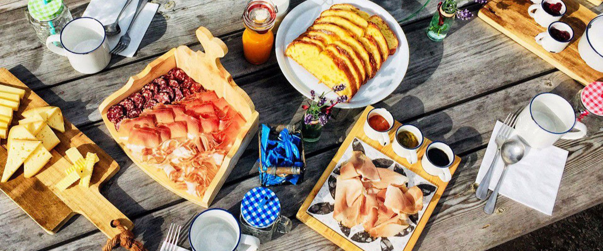 Tavolo da colazione con deliziosi pani, salumi, torte, bevande e marmellate.