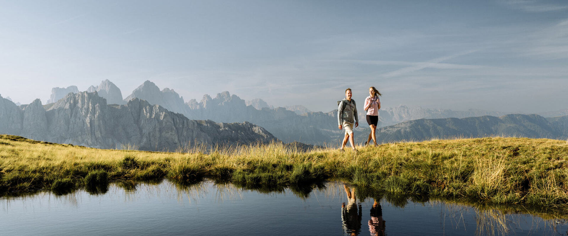 Escursionisti che si specchiano in un lago di montagna con le cime sullo sfondo