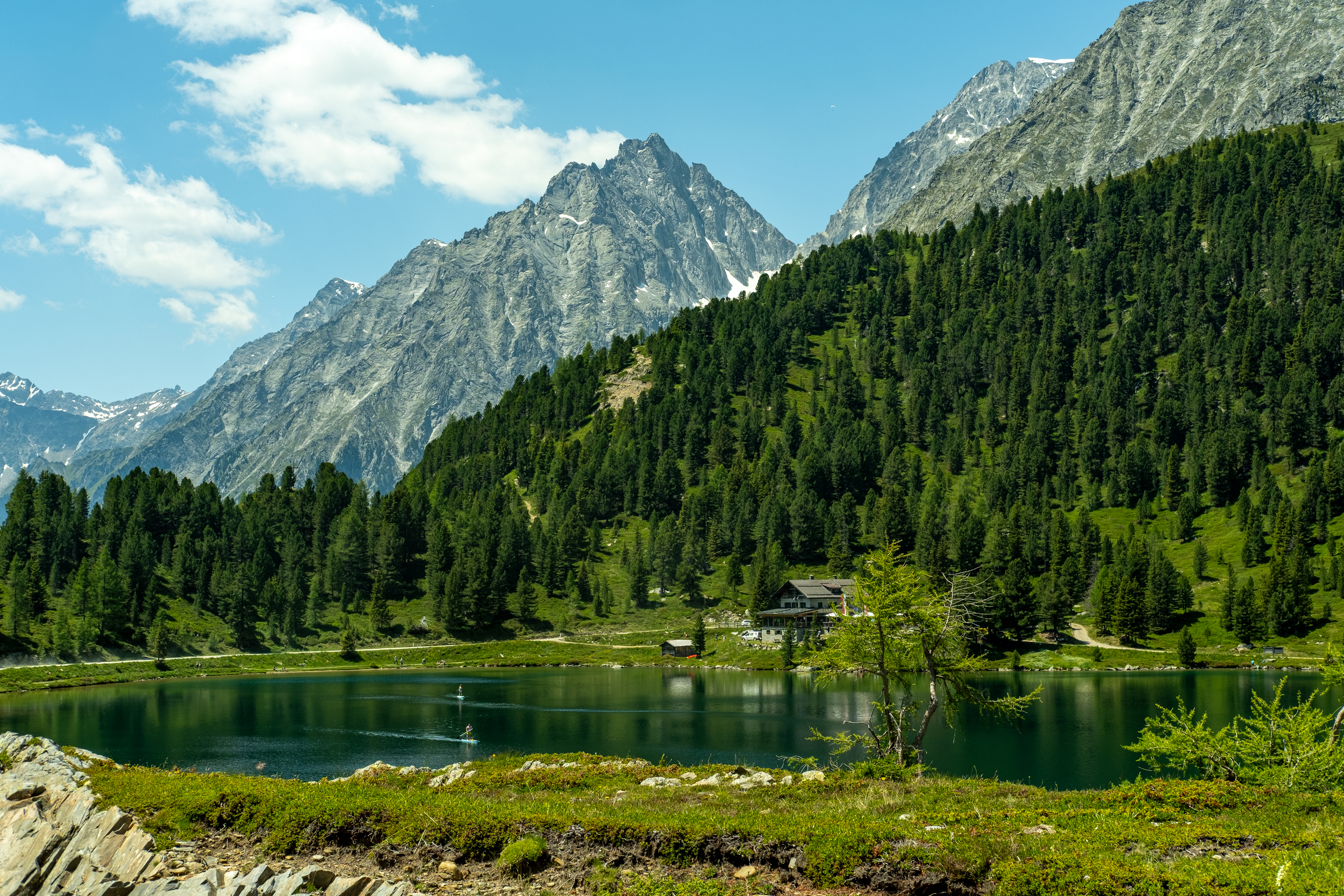Lago di montagna davanti a una baita, bosco e cime di montagna sul Passo Stalle