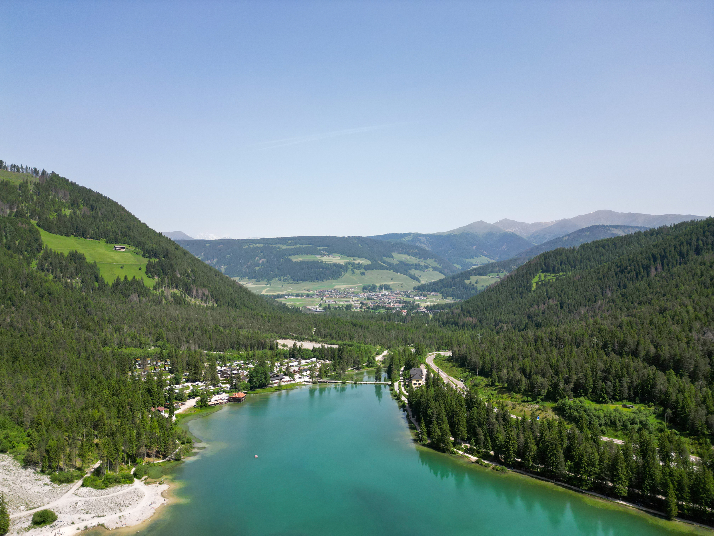 Lago incorniciato da boschi e campeggio, paesaggio montano con villaggio sullo sfondo