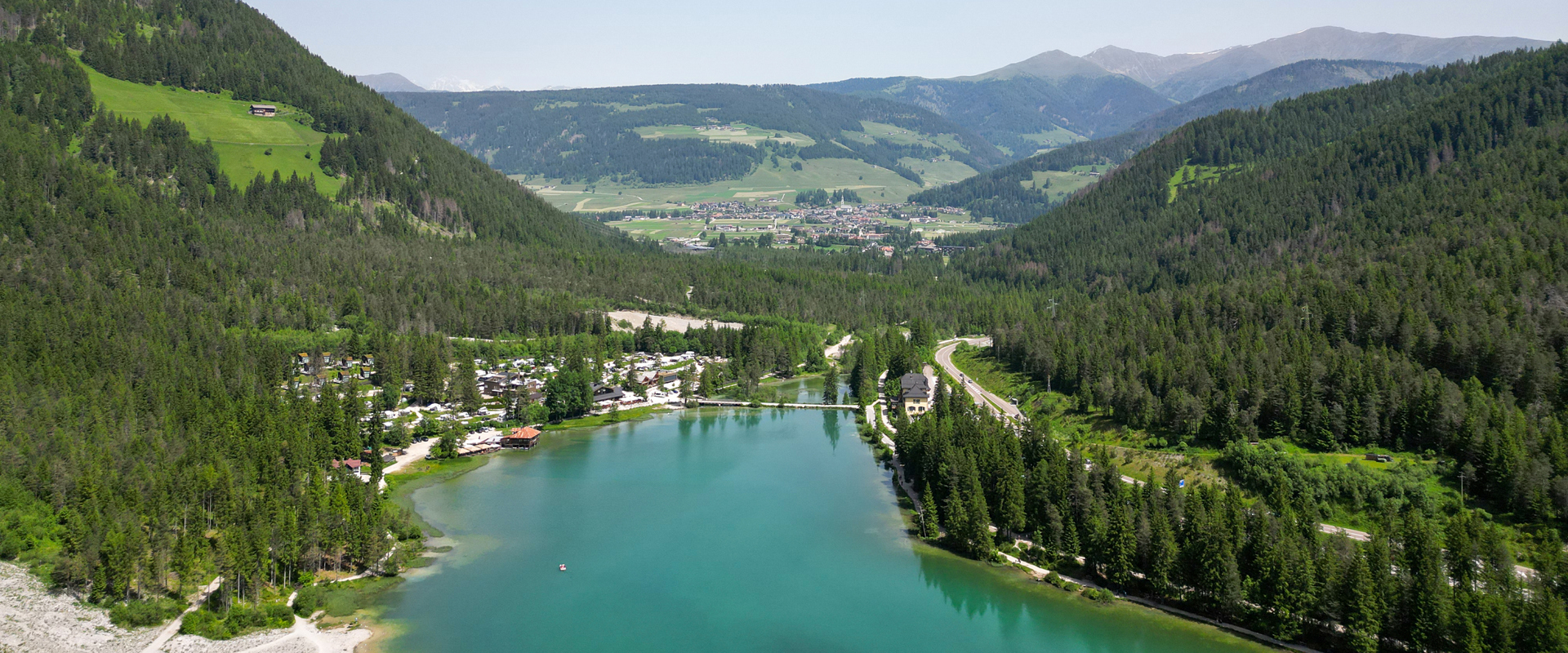 Lago di Dobbiaco Lago incorniciato da boschi e campeggio, paesaggio montano con villaggio sullo sfondo