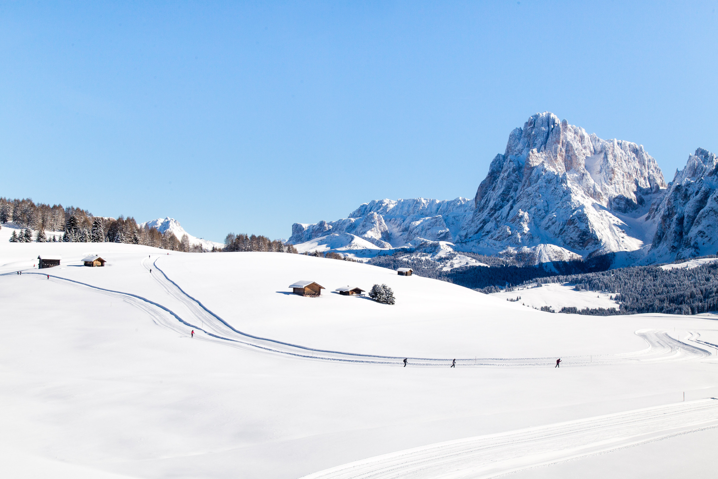 Sciatori di fondo su un altopiano innevato con rifugi alpini e panorama montano