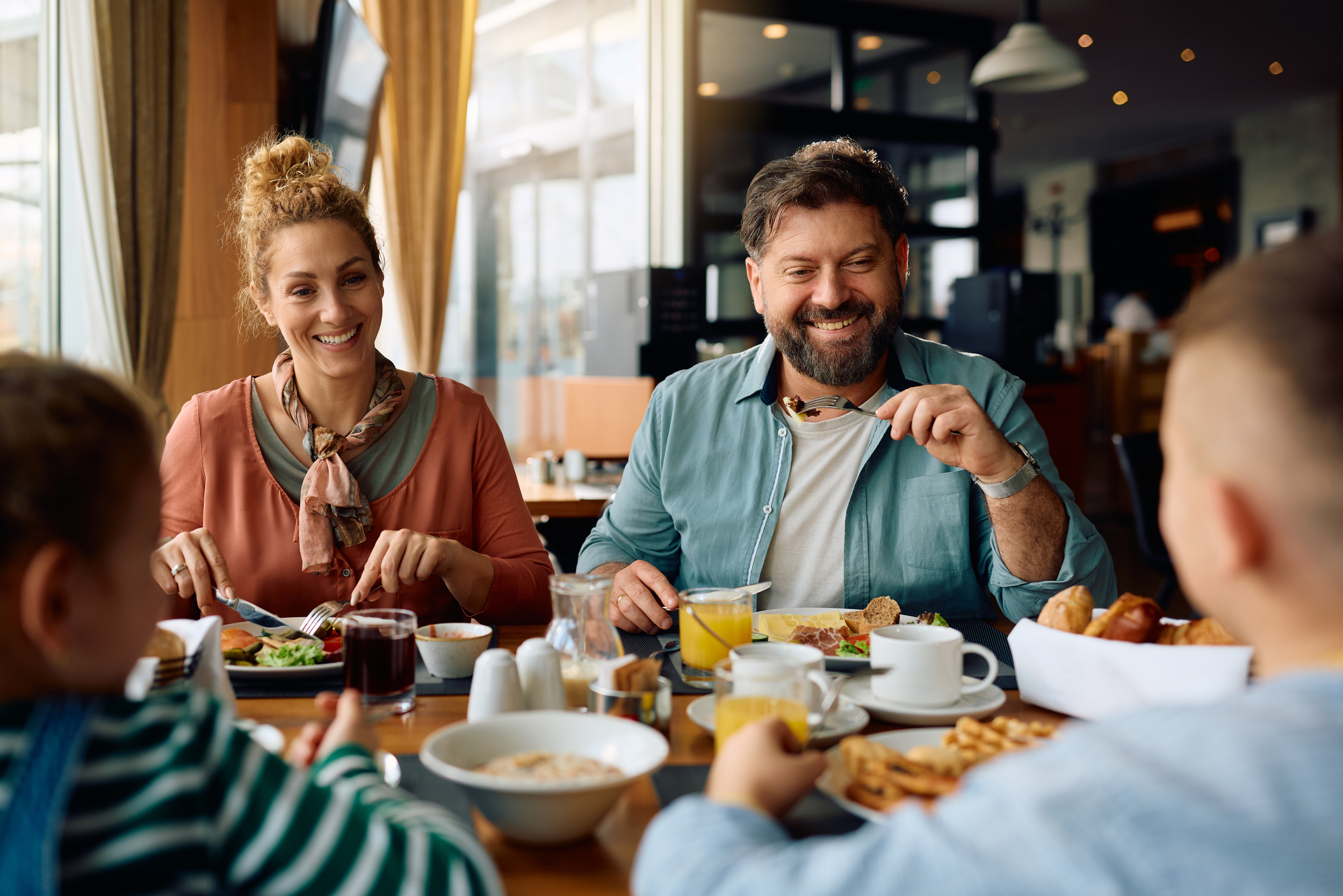 La famiglia è seduta al tavolo dell'hotel e fa colazione con caffè, pane e waffle
