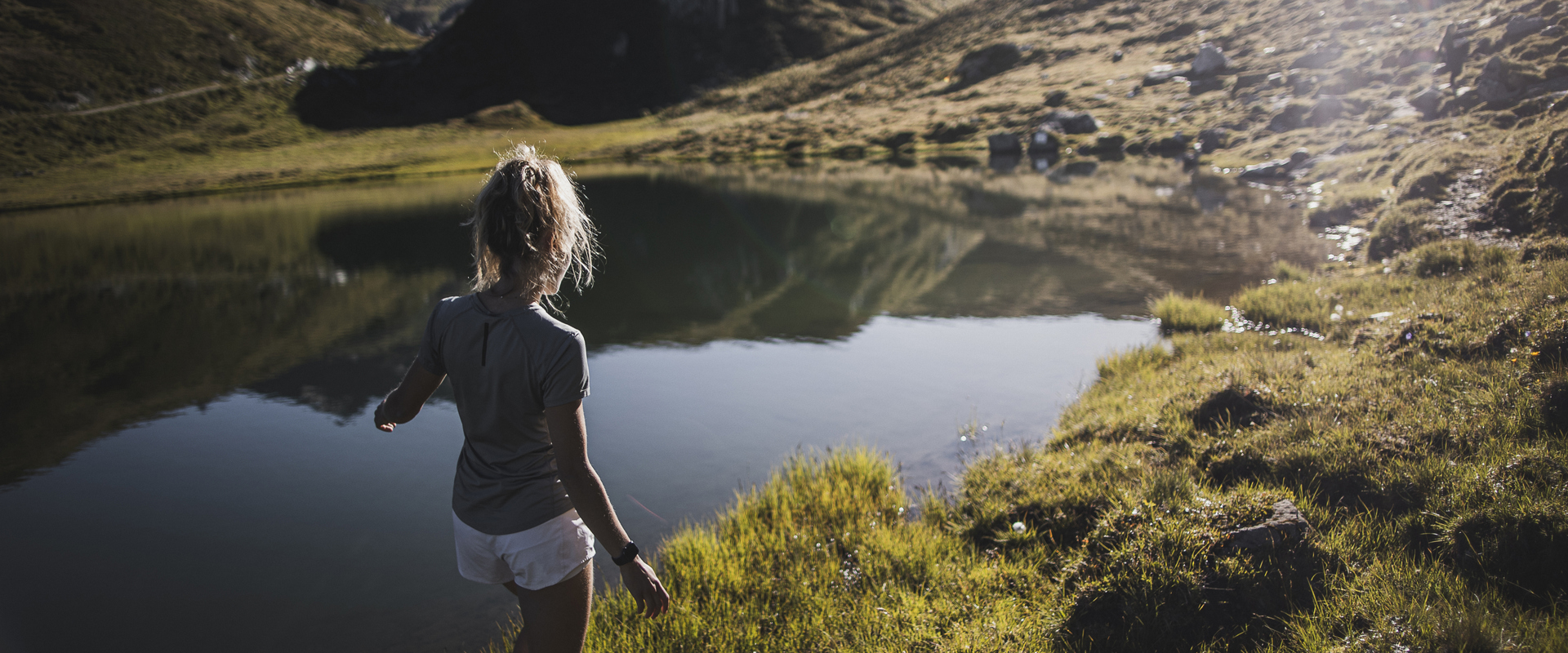Eine Frau geht durch das Gras am Ufer eines Südtiroler Bergsees.
