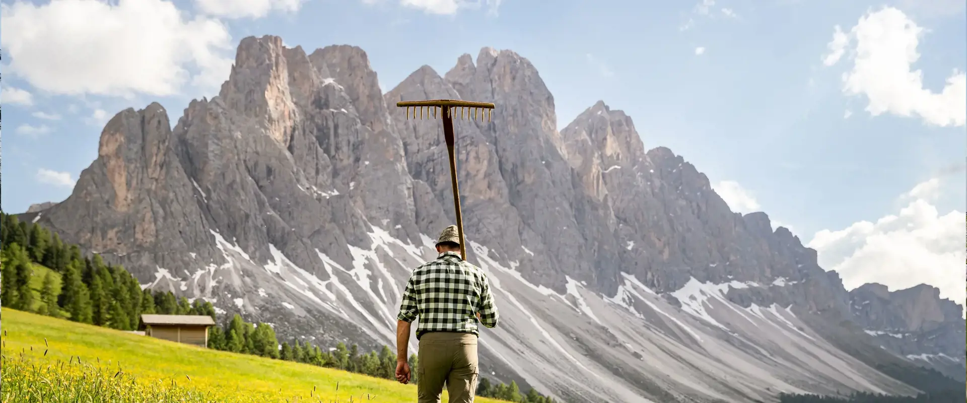 Contadino di montagna con forcone in un prato alpino.