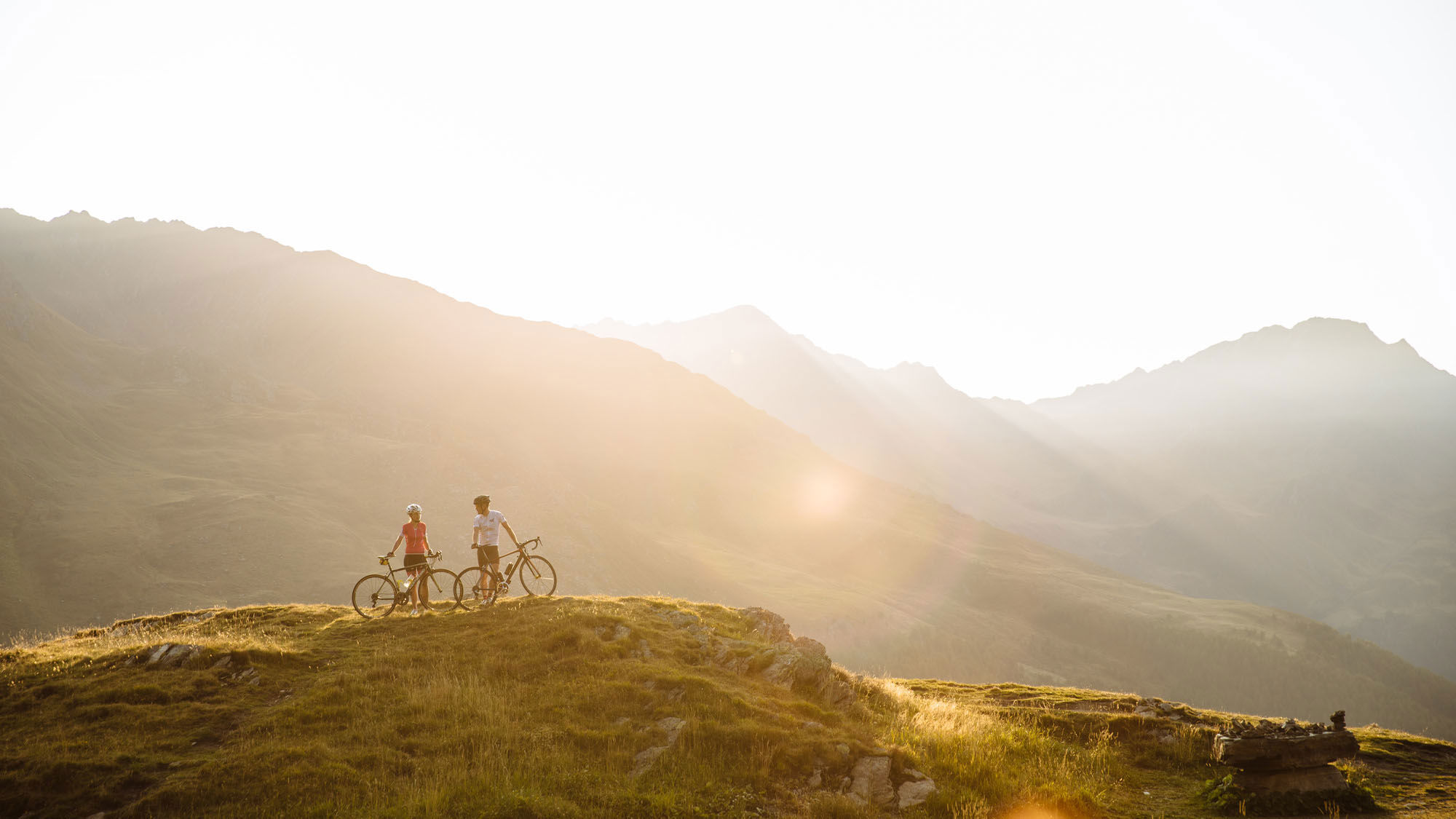 Due ciclisti si trovano su una collina con le loro biciclette e si godono il sole mattutino.