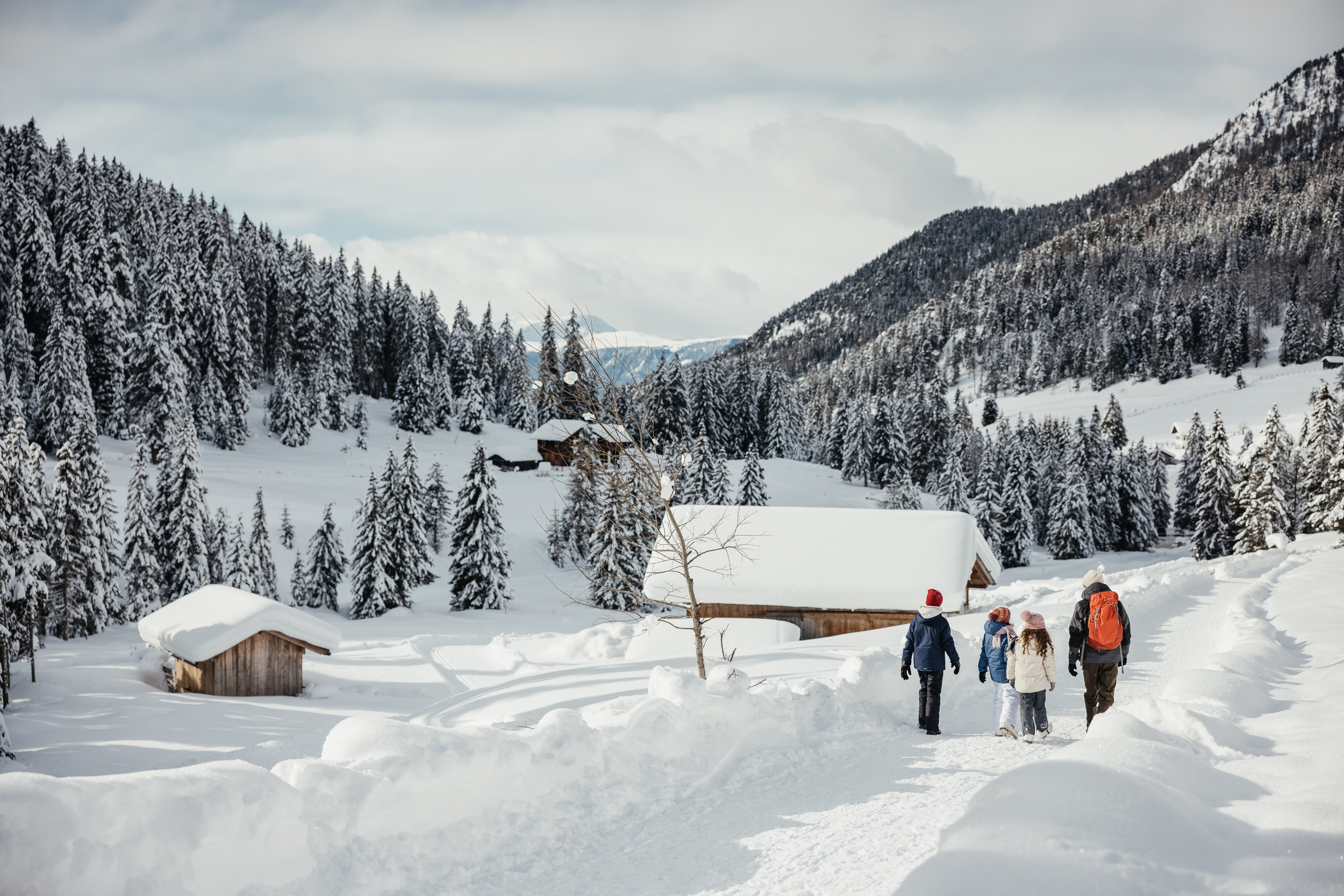 Escursione in famiglia su un sentiero invernale attraverso un paesaggio innevato con rifugi di montagna.