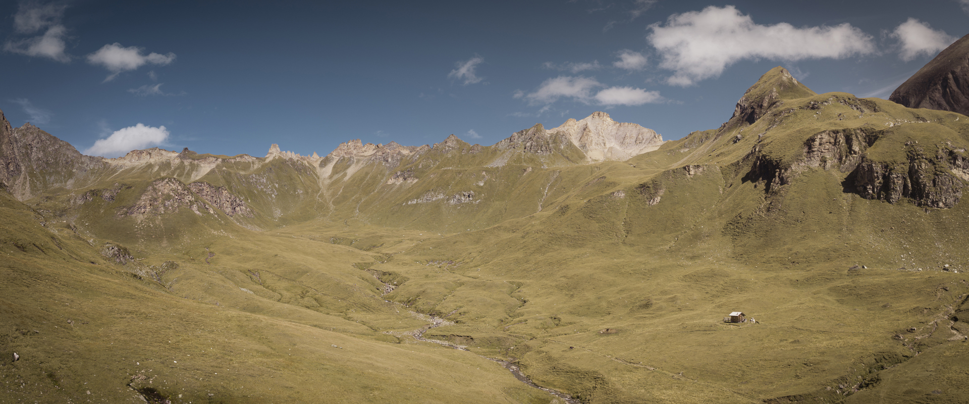 Dolci prati alpini, rifugi e cime montuose all'orizzonte